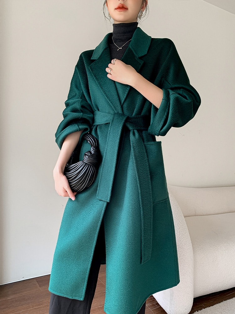 5397-dcjkcf.jpg Manteau long d'hiver en laine verte pour femme avec ceinture et col rabattu style manteau peignoir, porté par une mannequin debout avec un sac à main noir